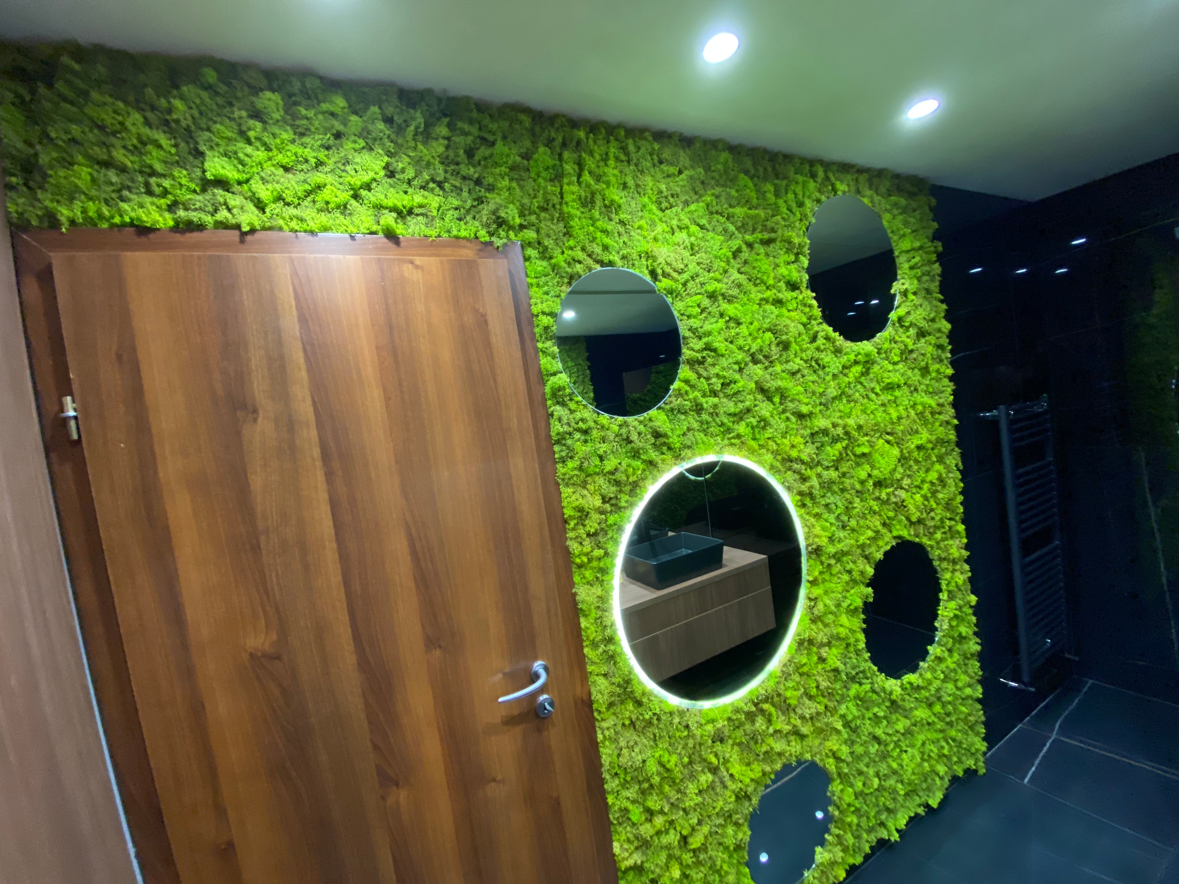 Perete decorativ cu licheni stabilizați verde natural și oglinzi rotunde integrate, montat in baie într-un spațiu modern.

