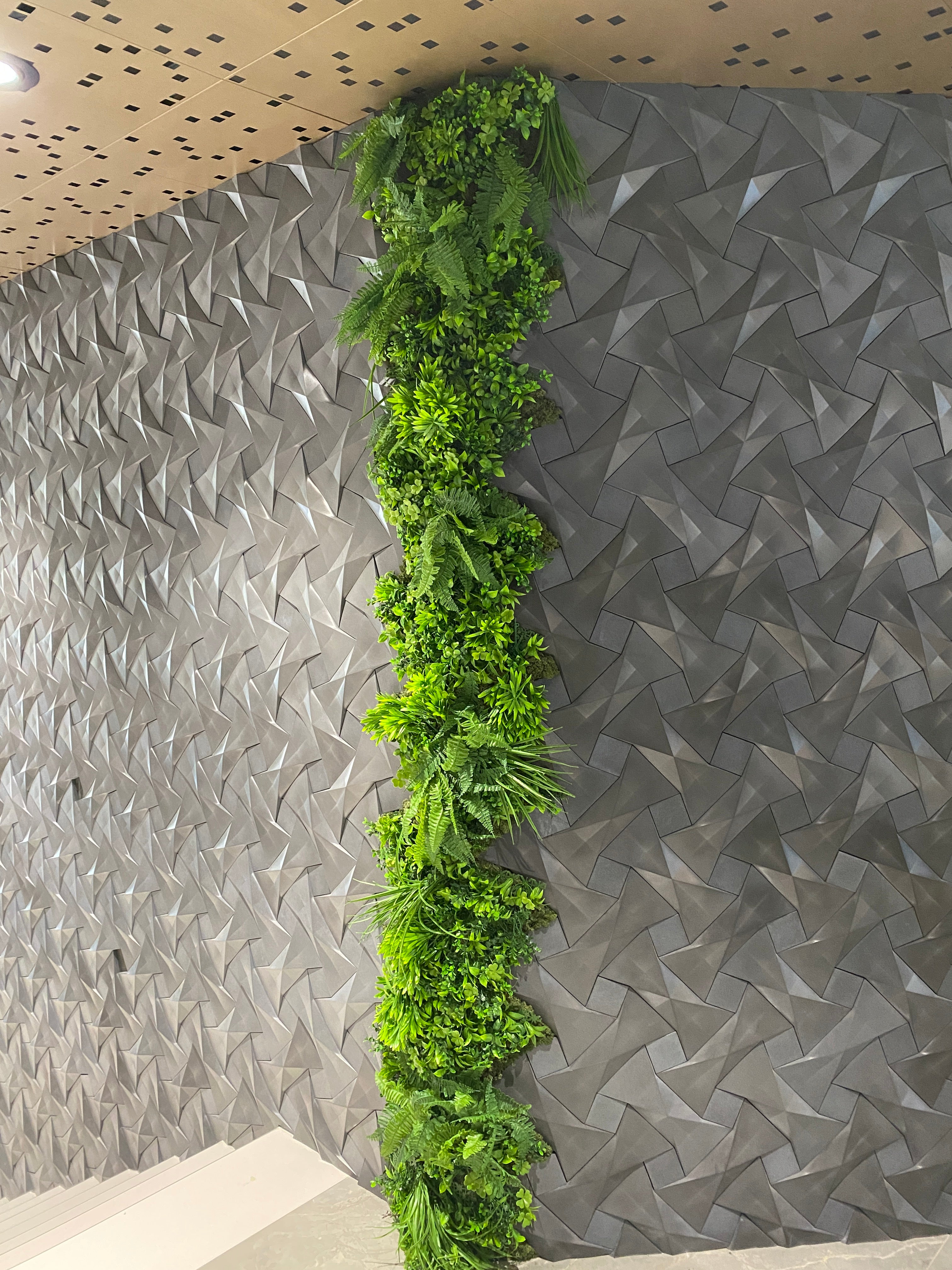 Perete verde artificial tip coloană verticală, realizat din plante sintetice, decor modern pentru spații interioare.
